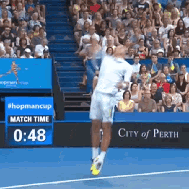a tennis player is jumping in the air during a match with a city of perth sign in the background