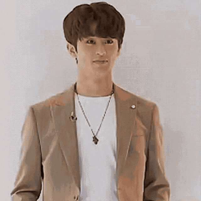 a young man wearing a tan suit jacket and a white shirt is standing in front of a white wall .