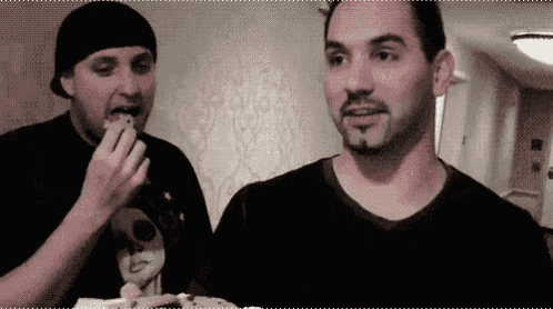 two men are eating hamburgers together in a room .