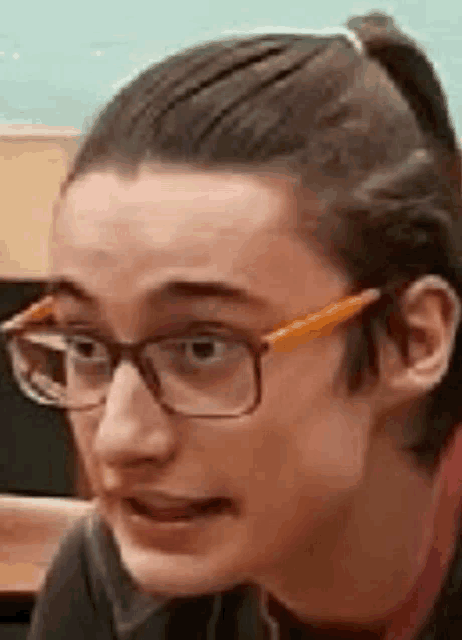 a young man wearing glasses and a ponytail is making a face .