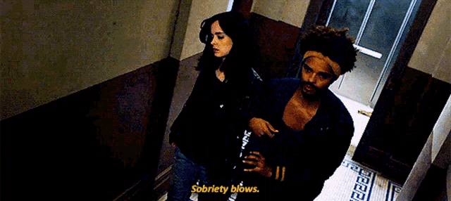 a man and a woman are standing next to each other in a hallway . the man is holding a glass of wine .