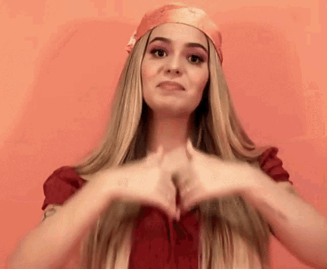 a woman with long blonde hair is making a heart with her hands