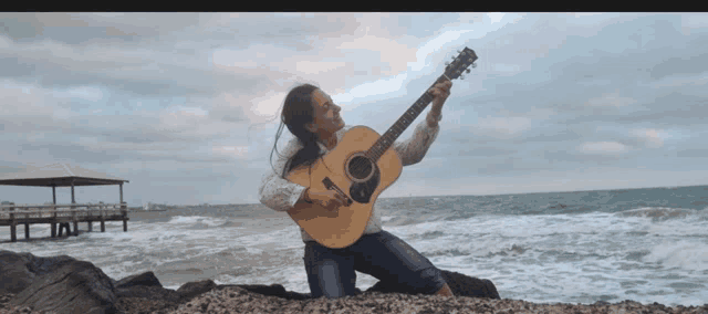 a woman is kneeling on a rock holding an acoustic guitar