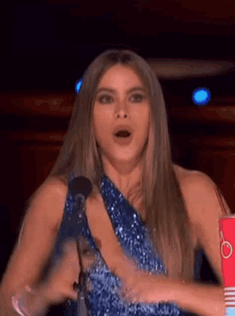 a woman in a blue dress is standing in front of a microphone and making a funny face .