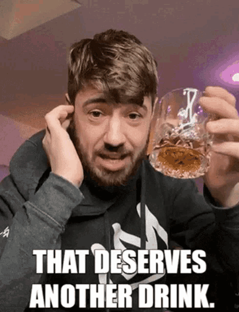 a man with a beard holds a glass of whiskey with the caption that deserves another drink