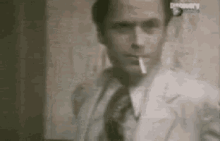a man is smoking a cigarette in a suit and tie .