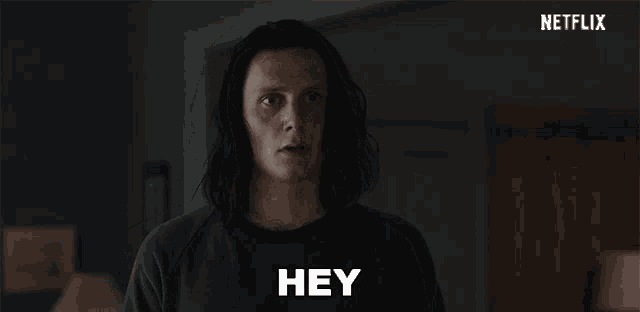 a man with long hair is standing in a dark room and making a funny face .