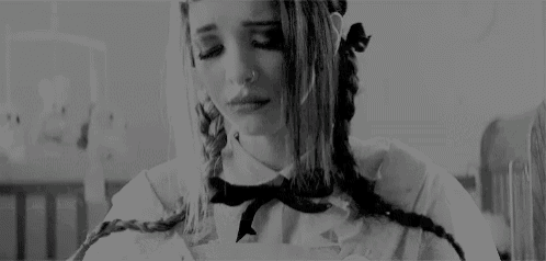 a black and white photo of a girl with braids and a nose ring crying .