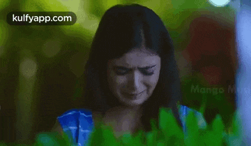 a woman is crying and covering her face with her hand while standing in front of a bush .