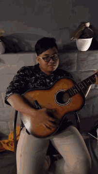 a man wearing glasses is playing an acoustic guitar on a bed