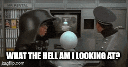 a man in a black helmet is talking to another man in a black helmet in front of a television .