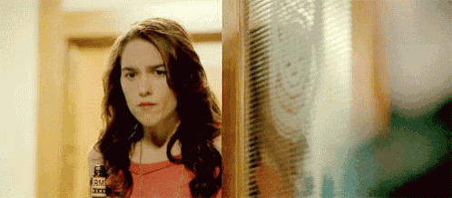 a woman in a red dress is standing in front of a door looking out .
