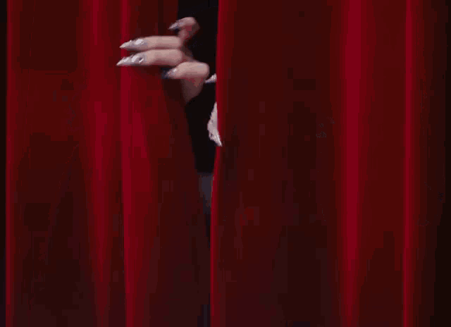 a close up of a woman behind a red curtain with confetti falling
