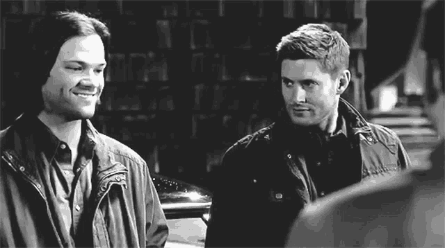 a black and white photo of two men standing next to each other and one of them is smiling .