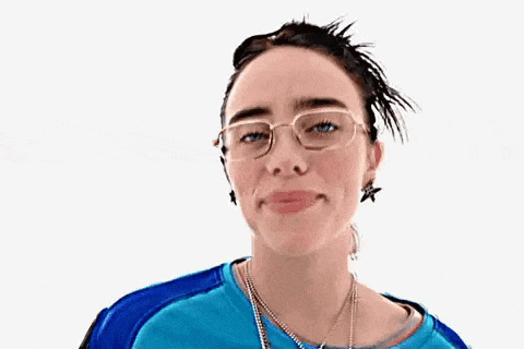 a woman wearing glasses , a blue shirt , a necklace , and a bun is smiling .