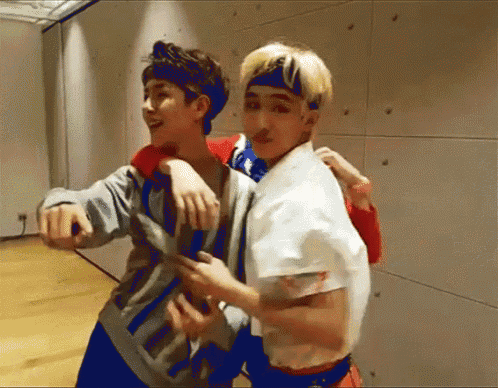 two young men are hugging each other in a room . one of the men is wearing a headband .
