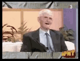a man in a suit and tie is sitting in front of a screen that says apht