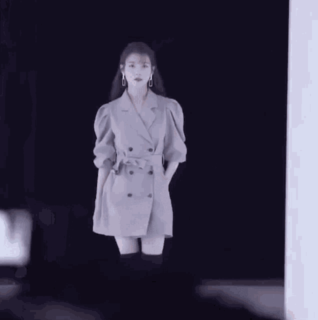 a woman in a trench coat and over the knee boots is standing in front of a black wall .