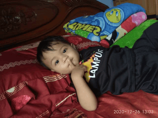 a little boy laying on a bed with a shirt that says lampung