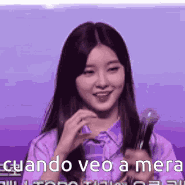 a woman in a purple shirt is holding a microphone in her hand and smiling .