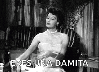 a woman in a dress is sitting at a table in a black and white photo and saying `` eres una damita '' .