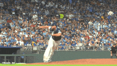 a baseball pitcher winds up to throw a ball in front of a crowd that is wearing blue