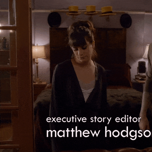 a woman in a robe is standing in a bedroom and the executive story editor is matthew hodgson
