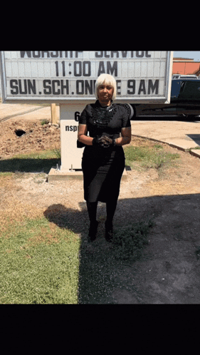 a woman in a black dress stands in front of a church sign that says 11:00 am