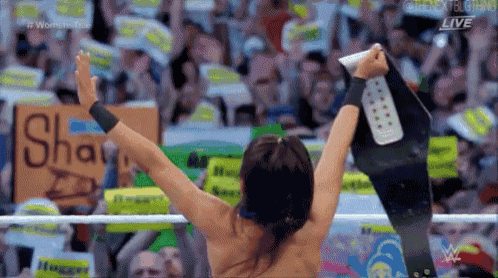 a wrestler is holding a championship belt in front of a crowd with a sign that says shaw on it