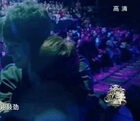 a man with green hair is hugging another man in front of a crowd in a dark room