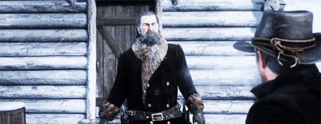 a man with a beard is standing in front of a log building