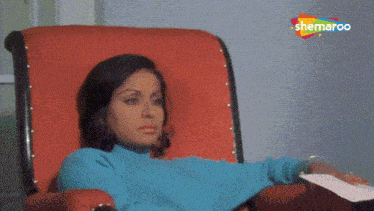 a woman in a blue sweater is sitting in an orange chair with a sherpao logo on the bottom