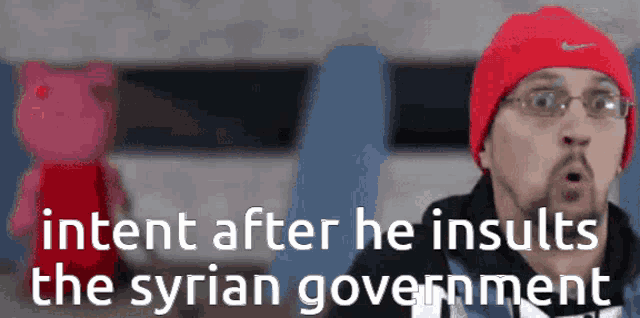a man wearing a red hat and glasses is talking about the syrian government