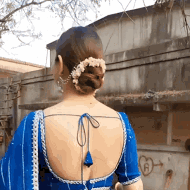 a woman wearing a blue blouse and a bun with flowers in her hair is standing in front of a building .