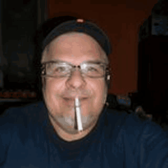a man wearing glasses and a hat is smoking a cigarette in his mouth .