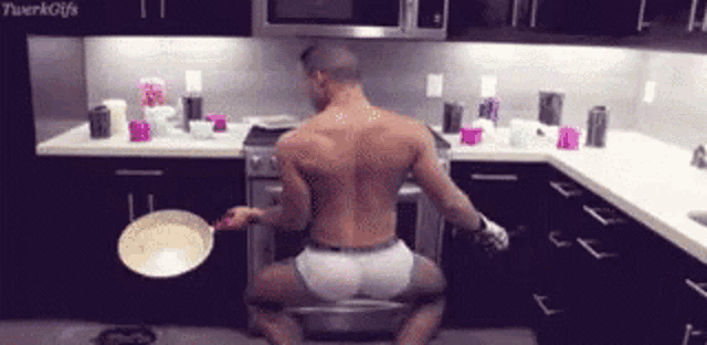 a shirtless man is kneeling down in a kitchen holding a pan