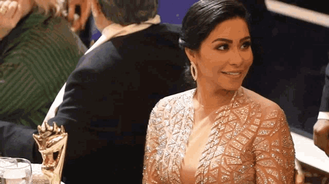 a woman in a gold dress is smiling while sitting next to a man in a suit