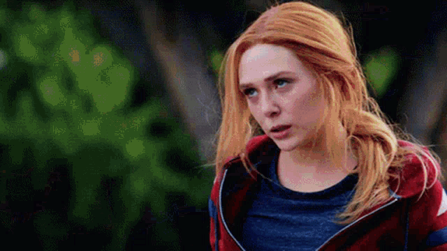 a close up of a woman with red hair wearing a red jacket and a blue shirt .