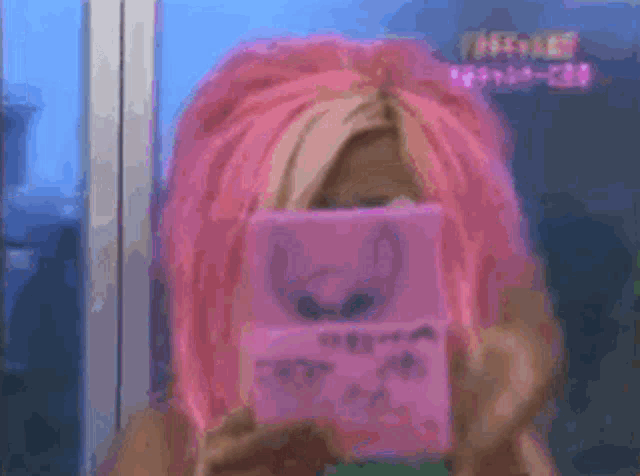 a woman with pink hair is covering her face with a pink box .