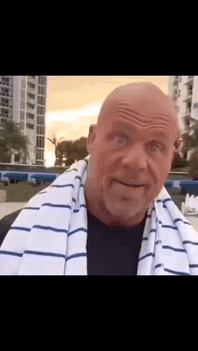 a bald man with a striped towel around his neck looks at the camera .