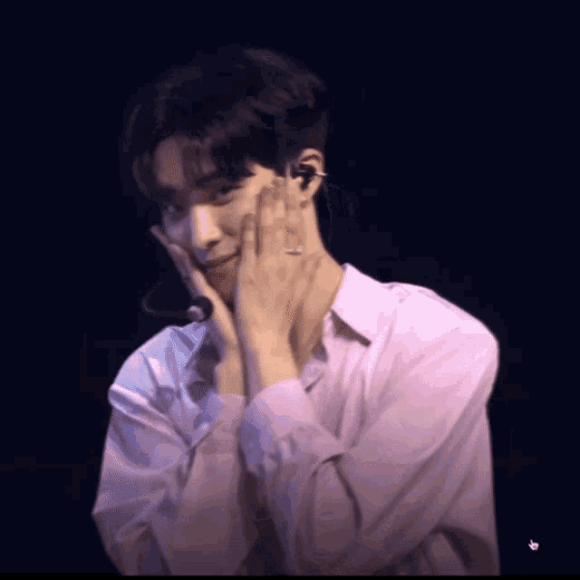 a man in a pink shirt is covering his face with his hands and smiling
