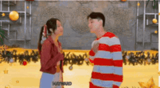 a man and a woman are standing next to each other and the man is wearing a red and white striped shirt .