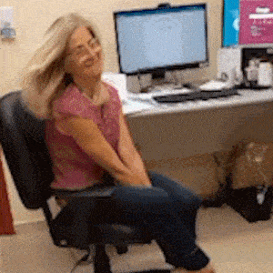 a woman sits in an office chair in front of a computer monitor