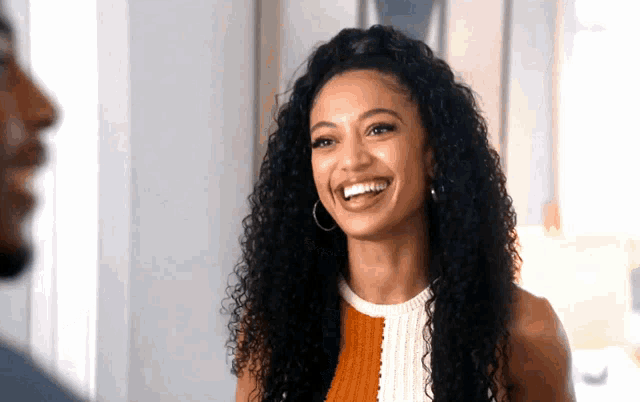 a woman with curly hair and hoop earrings smiles at a man