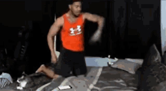 a man in an under armour tank top is standing on a bed .