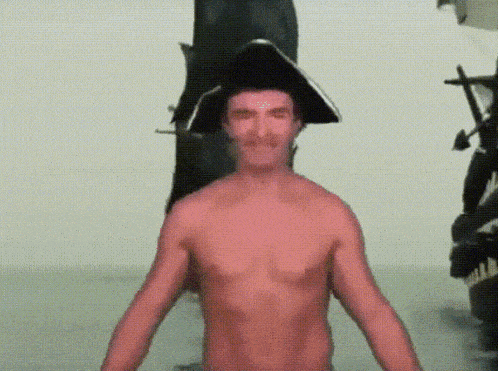 a shirtless man wearing a pirate hat is standing in front of a statue