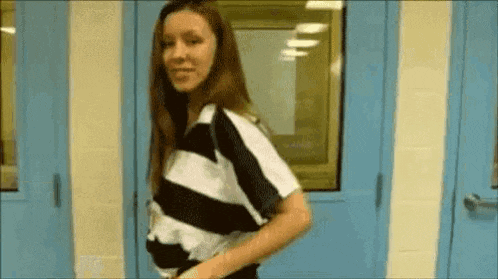 a woman in a striped shirt is standing in front of a blue door and smiling .