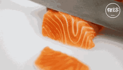 a knife is cutting a piece of salmon on a white plate .