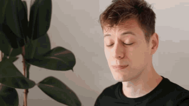 a young man with his eyes closed and a plant behind him