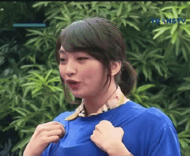 a woman in a blue shirt is standing in front of a tree with a transtv logo on the bottom